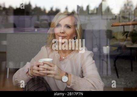 Portrait de femme blonde derrière le panneau de fenêtre à la maison Banque D'Images