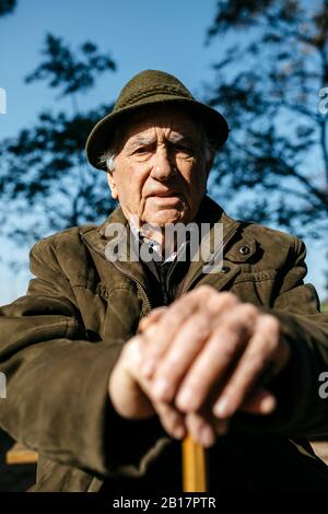 Vieil homme avec canne assise sur un banch dans un parc Banque D'Images