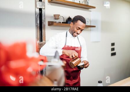 Barista souriant qui verse de la mousse de lait dans une tasse dans un café Banque D'Images