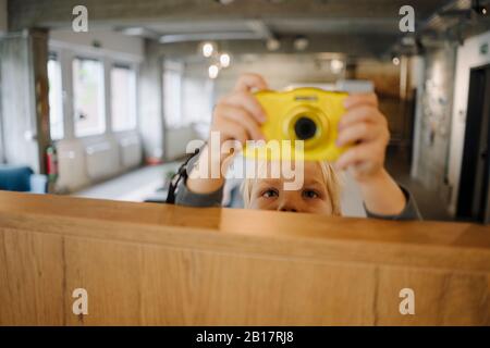 Garçon prenant une photo avec un appareil photo au bureau Banque D'Images