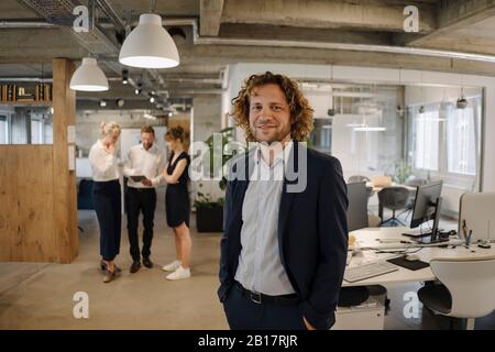 Portrait of smiling businessman in office avec des collègues en arrière-plan Banque D'Images