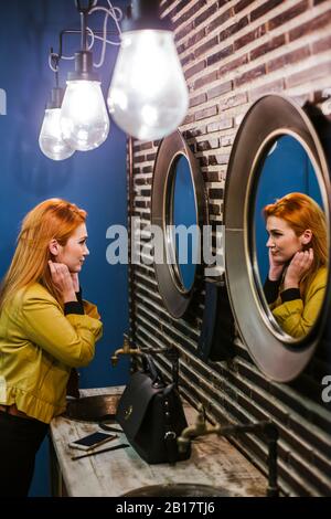 Jeune femme à tête rouge regardant son image miroir Banque D'Images