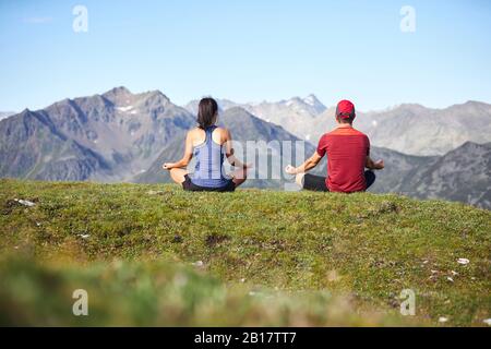 Homme et femme méditant dans les montagnes, vue arrière Banque D'Images