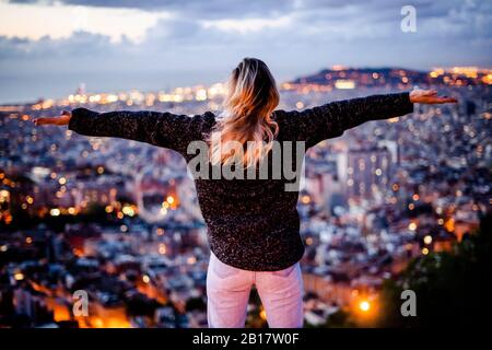 Jeune femme assise sur la rambarde au-dessus de la ville en utilisant un téléphone cellulaire, Barcelone, Espagne Banque D'Images