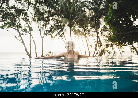 Femme dans la piscine à débordement au coucher du soleil, Nai Thon Beach, Phuket, Thaïlande Banque D'Images