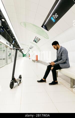 Jeune homme d'affaires avec scooter électrique et téléphone portable attendant dans la station de métro Banque D'Images