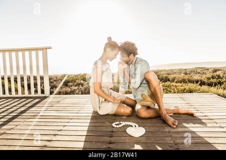 Affectueux jeune couple assis sur la terrasse sur la côte en été Banque D'Images