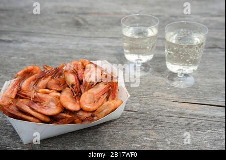 Boîte en carton de crevettes et deux tasses en plastique de vin blanc sur bois Banque D'Images