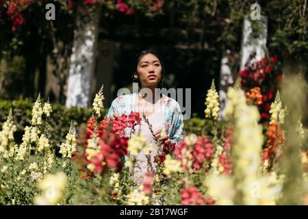 Jeune femme asiatique entourée de fleurs jouant avec des ombres sur son visage Banque D'Images