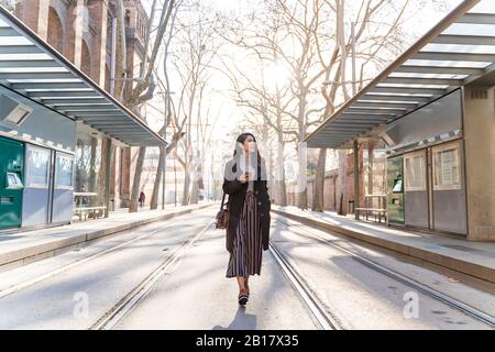 Jeune femme avec smartphone marchant sur la ligne de tram Banque D'Images