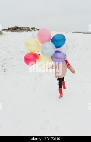 Vue arrière d'une fille avec des ballons qui s'enlisent sur une colline en hiver Banque D'Images