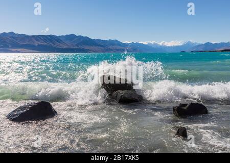 Nouvelle-Zélande, Océanie, Ile du Sud, Canterbury, Ben Ohau, Lac Pukaki et Alpes du Sud (Alpes de Nouvelle-Zélande) avec Aoraki / Mont Cook, vagues qui éclaboussent contre les rochers Banque D'Images