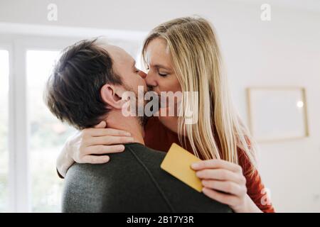 Heureux couple debout à la maison, baiser, tenant la carte de crédit Banque D'Images