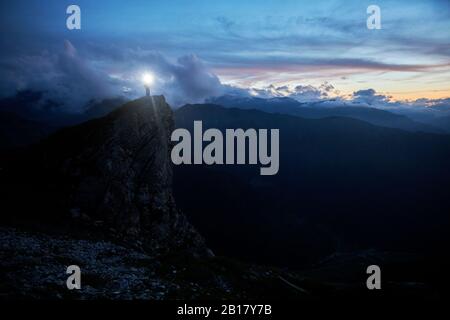 Randonneur debout sur l'éperon de roche au crépuscule, en regardant les montagnes Banque D'Images