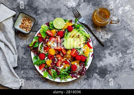 Studio de salade fruitée avec laitue agneaux, radicchio, coeurs de laitue, avocat, tomate, noix de pin, framboises, oranges, citron vert Banque D'Images