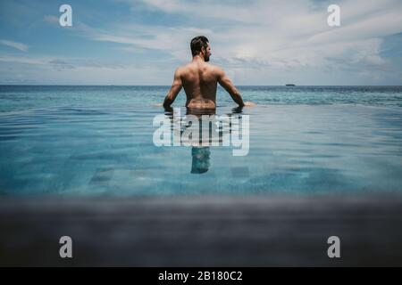 Vue arrière de l'homme se relaxant dans la piscine à débordement, l'île de Maguhdhuvaa, l'atoll de Gaafu Dhaalu, aux Maldives Banque D'Images