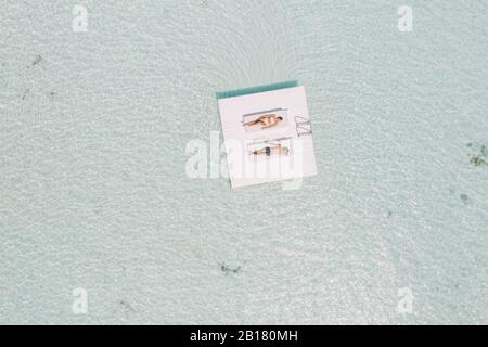 Couple allongé sur une plate-forme dans la mer, l'île de Maguhdhuvaa, l'atoll de Gaafu Dhaalu, Maldives Banque D'Images