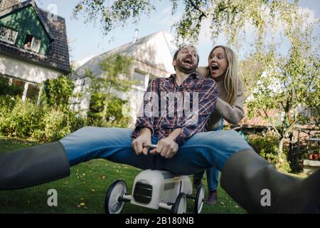 Rire couple prétendant monter une voiture jouet dans le jardin Banque D'Images