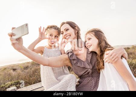 Une heureuse mère qui prend un selfie avec ses deux filles sur une promenade au coucher du soleil Banque D'Images