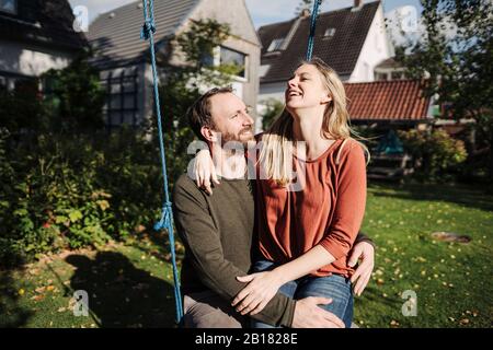 Couple affectueux assis sur swing dans leur jardin Banque D'Images