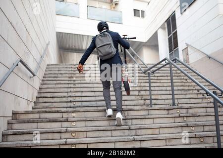 Vue arrière de l'homme d'affaires avec scooter poussant à l'étage Banque D'Images