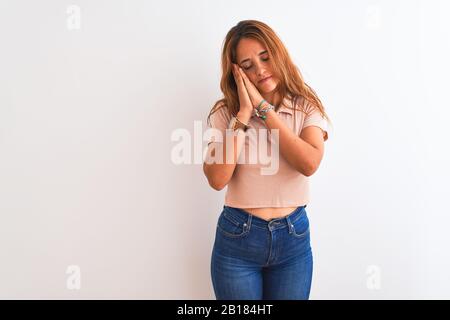 Jeune femme à tête rouge qui se promenait sur fond blanc isolé, dormant fatigué rêvant et se posant avec les mains tout en souriant avec des yeux fermés. Banque D'Images