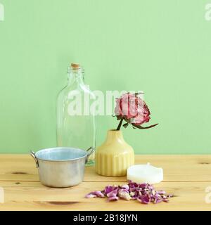 Objets d'aromathérapie. Bouteille de verre, fleur de rose séchée, bougie sur table en bois avec fond vert Banque D'Images