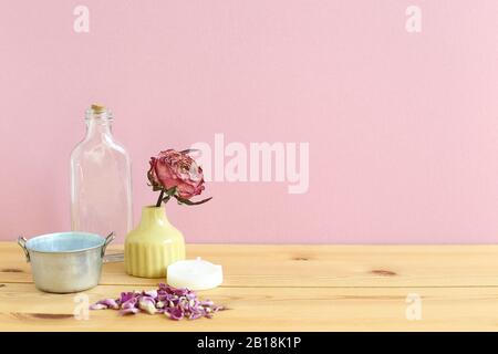 Objets d'aromathérapie. Bouteille de verre, fleur de rose séchée, bougie sur table en bois avec fond rose Banque D'Images