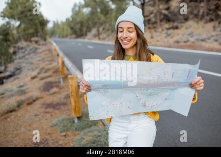 Portrait d'une jeune femme élégante avec carte papier sur le côté de la route, se déplaçant dans la forêt Banque D'Images