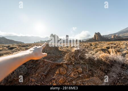 Femme pointant à la main sur les montagnes volcaniques pendant un coucher de soleil, l'image se focalise sur l'arrière-plan Banque D'Images