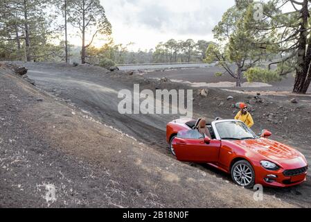 Femme voyageant par un cabriolet rouge, debout sur la route de la terre volcanique, vue large Banque D'Images