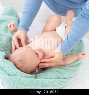 Massage du visage de bébé. Mère strobant doucement le visage de bébé avec les deux mains. Gros plan. Banque D'Images