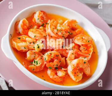 Crevettes à l'ail et au beurre saupoudrées de persil servi sur une plaque rose sur fond de bois blanc, orientation horizontale, gros plan Banque D'Images