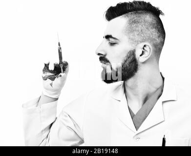 Concept de travail professionnel et de médecine: Médecin avec barbe sombre et expression concentrée du visage regarde la seringue dans sa main, qui est tachée de sang, isolée sur fond blanc Banque D'Images