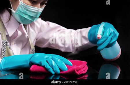 femme porter un masque hygiénique , utiliser un gant en caoutchouc bleu tenant un chiffon de nettoyage en microfibre rose et vaporiser une solution de stérilisation faire le nettoyage et Banque D'Images