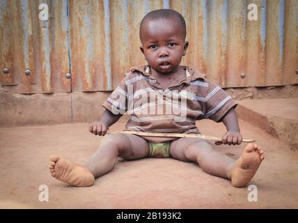 Kibera, Nairobi, Kenya - 13 février 2015 : un petit enfant noir sale est assis sur le sol dans les bidonvilles et tient un bâton dans ses mains Banque D'Images