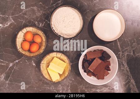 Le beurre coupé en dés pour faire brownie fait maison ingrédients près de chocolat, poudre de cacao, farine, œufs, noix et sucre, vue d'en haut. Banque D'Images