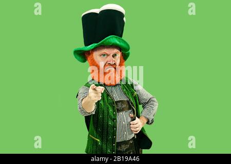 Pointage, choix. Lepreun excité en costume vert avec barbe rouge sur fond vert. Portrait drôle de l'homme prêt pour les ventes. Saint Patrick jour, émotions humaines, célébration, vacances traditionnelles. Banque D'Images