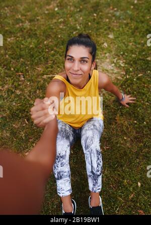 vue haute d'une jeune femme souriante de forme physique assise sur l'herbe verte tenant fermement sa main d'amis féminins - ami offrant une main d'aide Banque D'Images