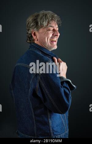 Portrait d'un homme avec une veste denim bleue riant sur fond dégradé Banque D'Images