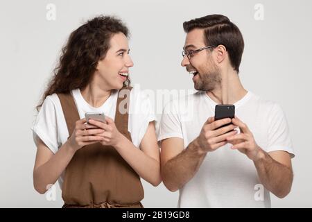 Un jeune couple enchanté et enchanté se regardant les uns les autres, tenant des téléphones mobiles. Banque D'Images