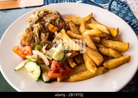 Poulet cuit au four avec frites et légumes sur une plaque blanche et une nappe bleue. Banque D'Images