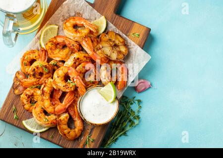 Brochettes de crevettes grillées ou langoustines servies avec de la chaux, de l'ail et de la sauce sur fond de béton bleu clair. Fruits de mer et bière. Vue de dessus avec copie Banque D'Images