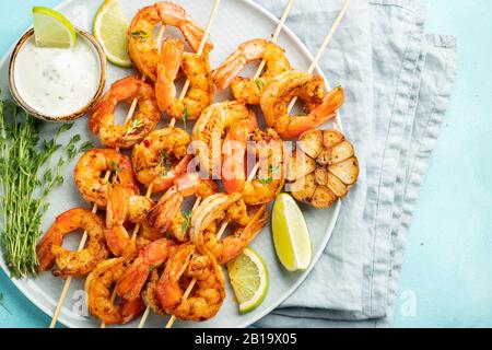 Brochettes de crevettes grillées ou langoustines servies avec de la chaux, de l'ail et de la sauce sur fond de béton bleu clair. Fruits de mer et bière. Vue de dessus. Pose à plat Banque D'Images