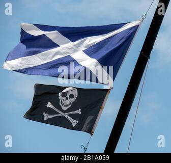 Mât de navires sur la plage de Tresaith montrant le drapeau national écossais soufflé par le vent et le crâne et les croisillons ou connu sous le nom de Jolly Roger drapeau Banque D'Images