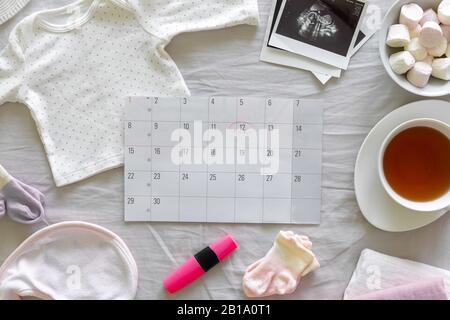 Calendrier avec la date prévue de naissance du bébé, différents vêtements de bébé et échographie, grossesse et concept de naissance Banque D'Images