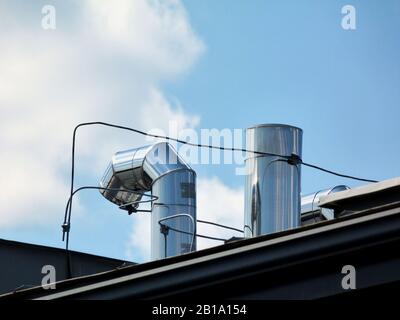 conduits et aérateurs mécaniques en tôle d'acier inoxydable brillant sur toit incliné. ingénierie du bâtiment, chauffage, refroidissement et système de ventilation du bâtiment. Banque D'Images