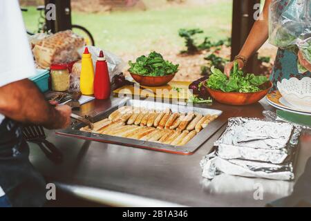 Les gens qui préparent la nourriture pour la fête, cuisinant des saucisses sur barbecue et servent une salade verte. Barbecue public en Australie. Pique-nique dans le parc. Banque D'Images