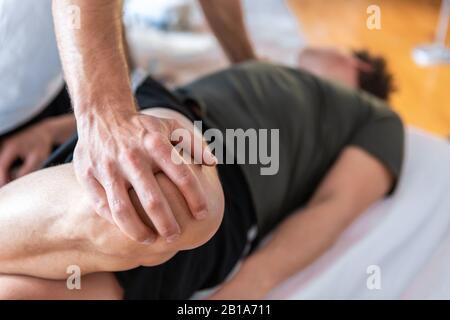 Gros plan d'un masseur professionnel offrant un massage des jambes à un homme fort allongé dans le centre thermal. Focalisation sélective sur les mains Banque D'Images