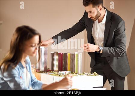 homme barbu en costume noir élégant mesurant la disposition tandis que son collègue travaillant avec une paire de compas au premier plan flou Banque D'Images